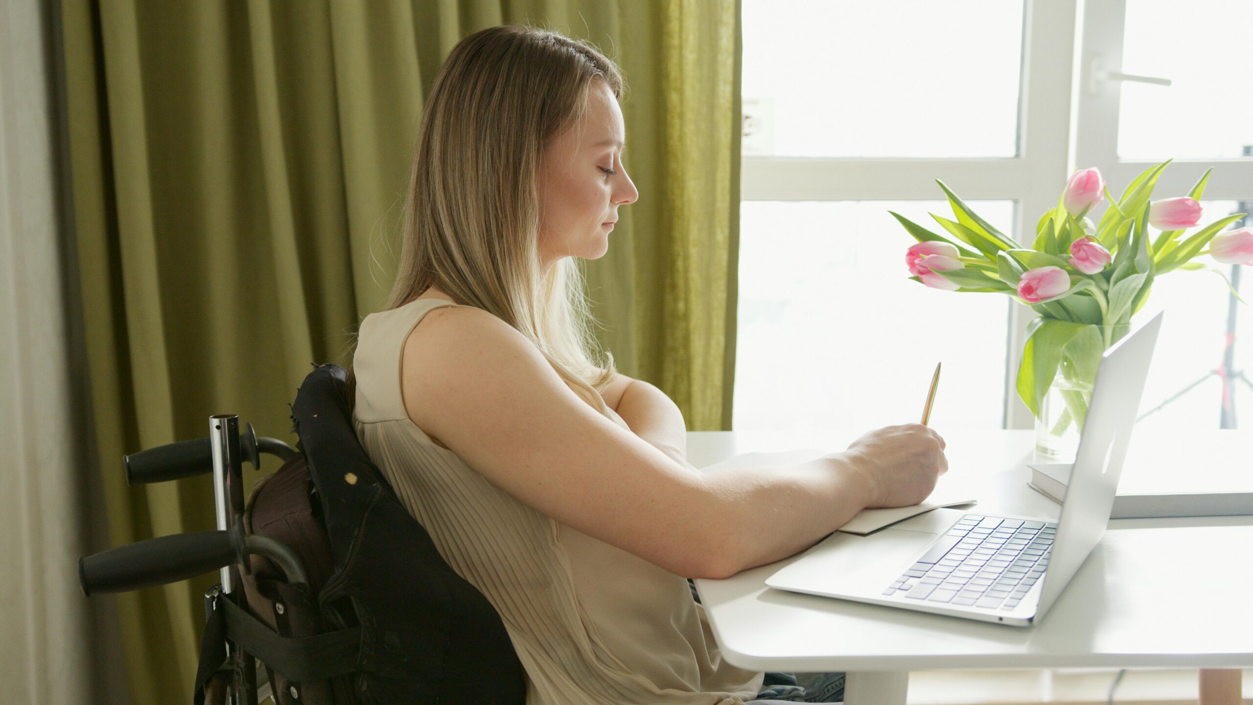 Blonde Frau im Rollstuhl sitzt am Laptop am Tisch